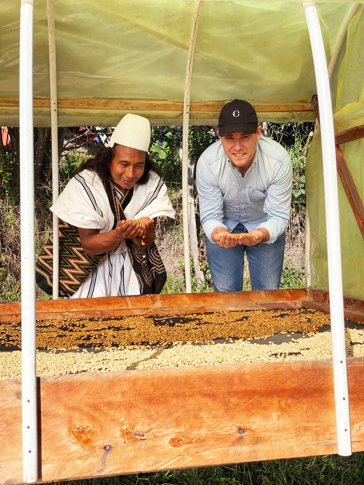 A grower and a member of the CRU Kafe team inspecting parchment coffee on the drying beds